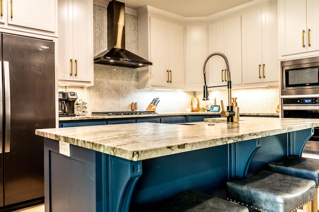 kitchen featuring light stone counters, wall chimney range hood, a kitchen breakfast bar, and appliances with stainless steel finishes