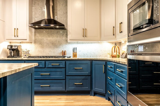 kitchen with white cabinetry, wall chimney exhaust hood, stainless steel appliances, and blue cabinets