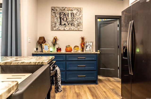 kitchen with black fridge with ice dispenser, blue cabinetry, and light hardwood / wood-style floors