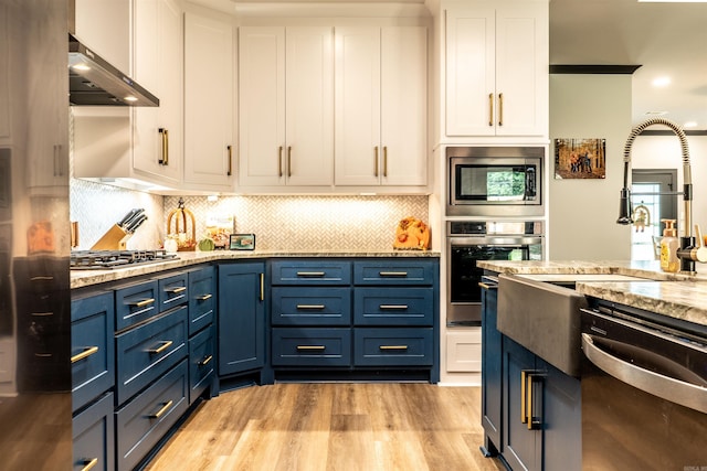 kitchen featuring stone counters, appliances with stainless steel finishes, range hood, white cabinetry, and blue cabinetry