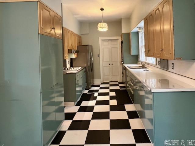 kitchen featuring light brown cabinetry, hanging light fixtures, stainless steel fridge, and sink