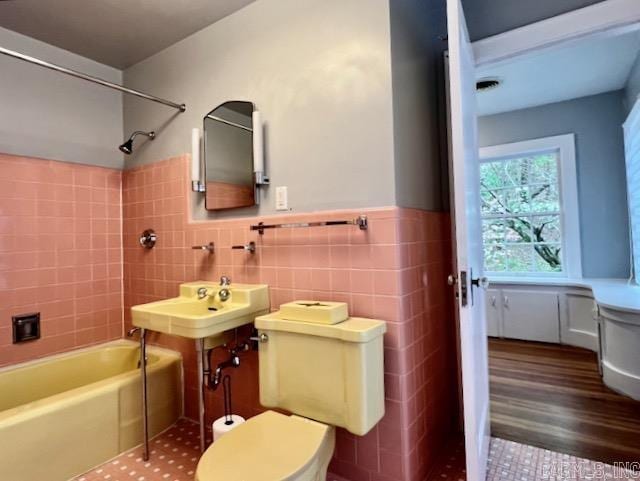 bathroom featuring tiled shower / bath combo, tile walls, and toilet