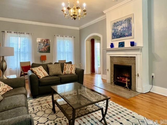 living room featuring an inviting chandelier, ornamental molding, a wealth of natural light, and light hardwood / wood-style floors