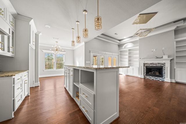 kitchen with white cabinetry, a kitchen island with sink, light stone counters, and decorative light fixtures