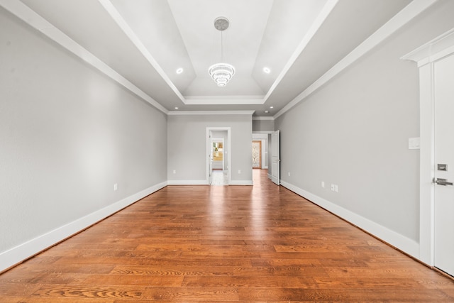 spare room featuring hardwood / wood-style flooring, ornamental molding, a raised ceiling, and a notable chandelier