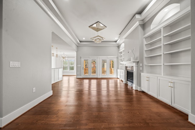 unfurnished living room with crown molding, built in features, dark hardwood / wood-style floors, and a chandelier