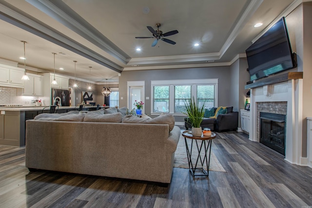 living room featuring ornamental molding, a tray ceiling, dark hardwood / wood-style flooring, and ceiling fan with notable chandelier