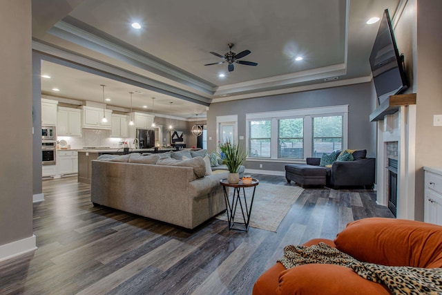 living room featuring a raised ceiling, ornamental molding, dark wood-type flooring, and ceiling fan