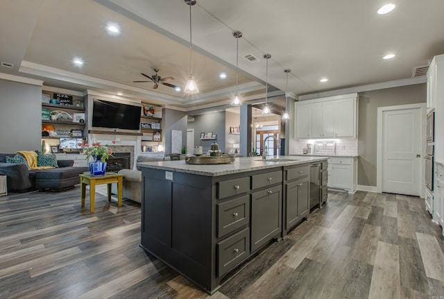 kitchen featuring sink, decorative light fixtures, a center island with sink, a tray ceiling, and white cabinets