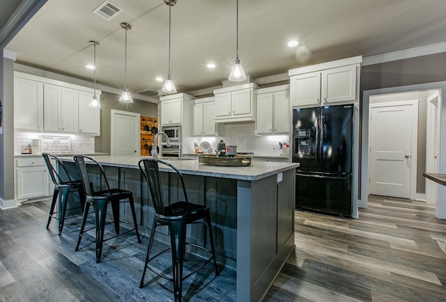 kitchen featuring hanging light fixtures, black fridge, stainless steel microwave, and a center island with sink