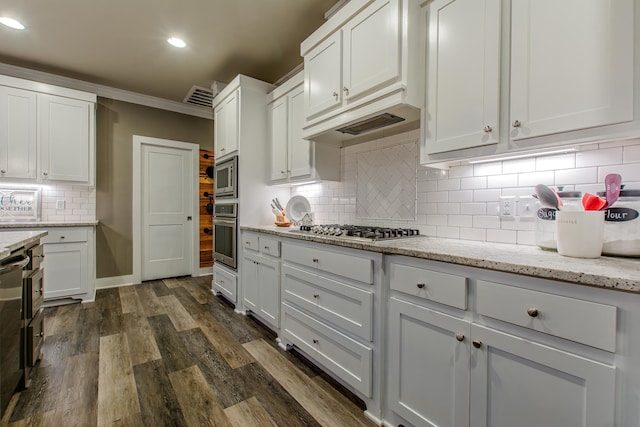 kitchen with appliances with stainless steel finishes, dark hardwood / wood-style floors, white cabinets, light stone countertops, and backsplash