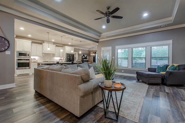 living room with dark hardwood / wood-style flooring, a tray ceiling, ceiling fan with notable chandelier, and ornamental molding