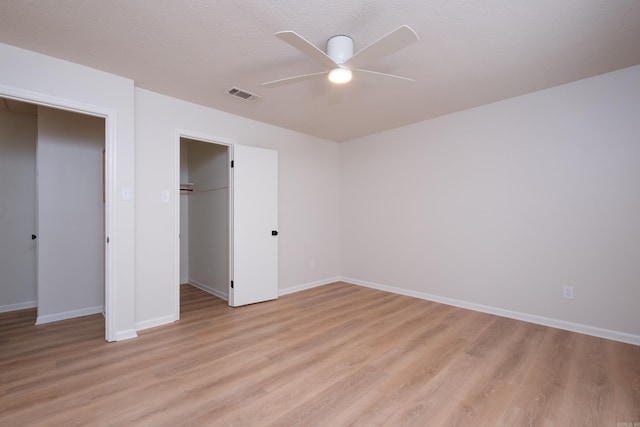 unfurnished bedroom with ceiling fan, light hardwood / wood-style floors, a textured ceiling, a walk in closet, and a closet