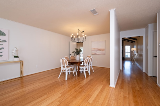 unfurnished dining area with an inviting chandelier, ornamental molding, a textured ceiling, and light wood-type flooring