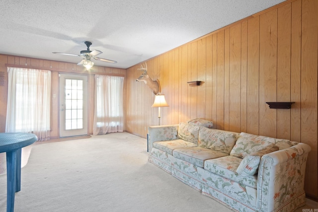 carpeted living room with ceiling fan, wooden walls, and a textured ceiling