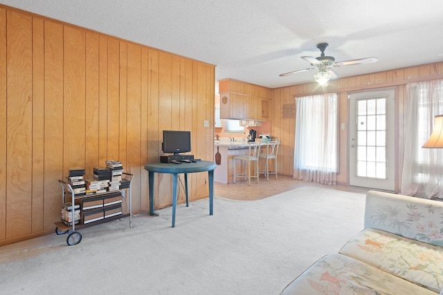 living room with light carpet, a textured ceiling, ceiling fan, and wood walls