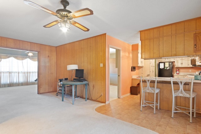 kitchen featuring a breakfast bar, light carpet, black refrigerator, wooden walls, and kitchen peninsula