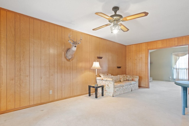 unfurnished living room with wooden walls, light colored carpet, and ceiling fan