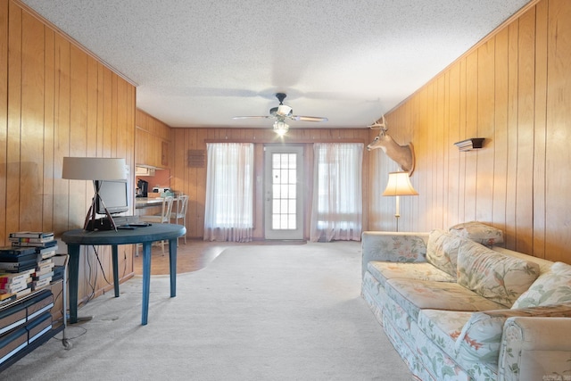 carpeted living room featuring ceiling fan, wooden walls, and a textured ceiling