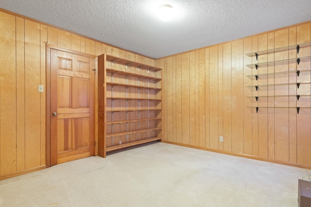 unfurnished room featuring light colored carpet, a textured ceiling, and wood walls