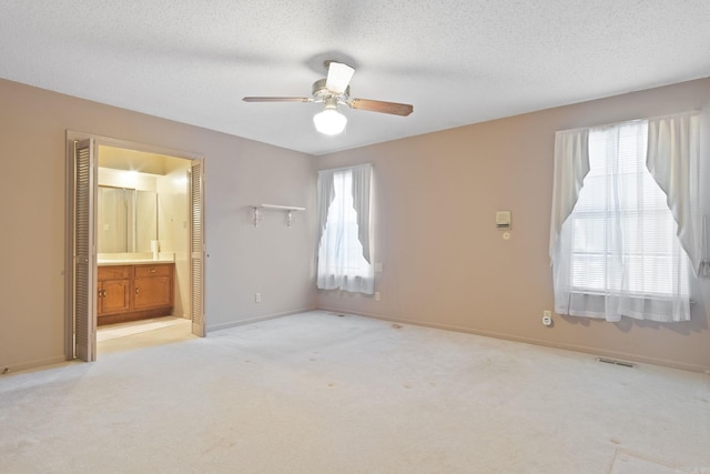 unfurnished bedroom featuring ceiling fan, light carpet, a textured ceiling, and ensuite bath