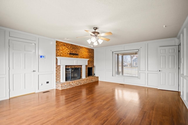 unfurnished living room featuring wood-type flooring, ceiling fan, crown molding, a brick fireplace, and a textured ceiling