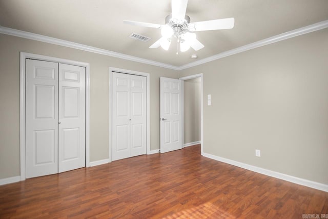 unfurnished bedroom with hardwood / wood-style floors, ornamental molding, two closets, and ceiling fan