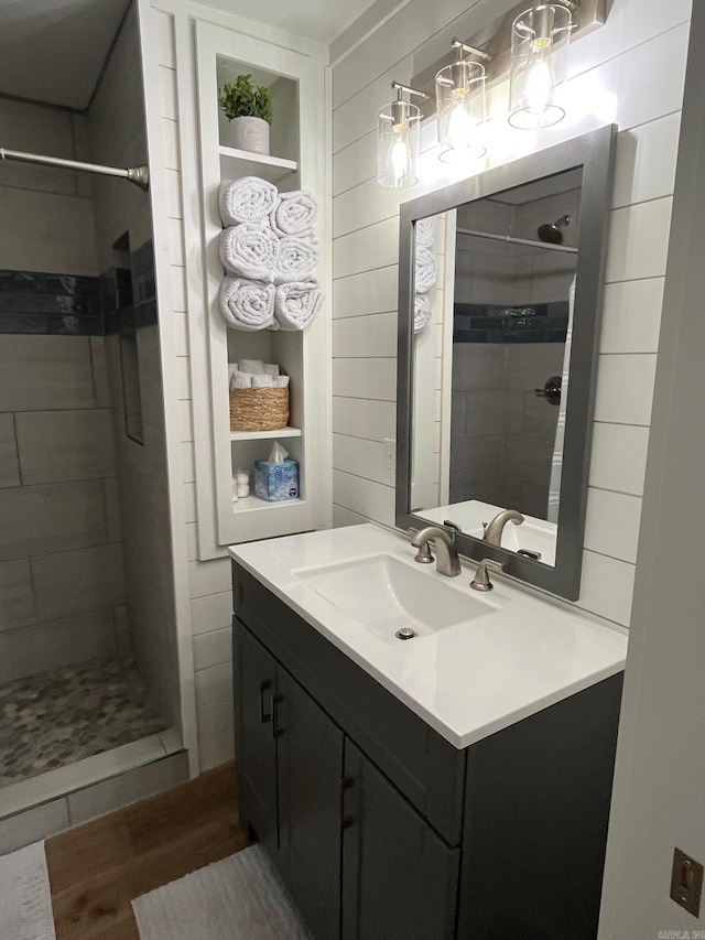 bathroom featuring a tile shower, vanity, and wooden walls