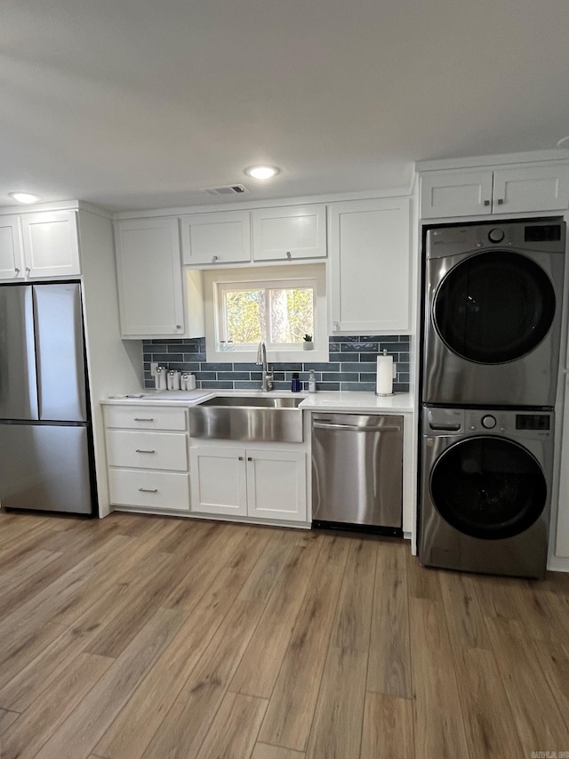 kitchen with sink, white cabinets, stacked washer and clothes dryer, stainless steel appliances, and light wood-type flooring