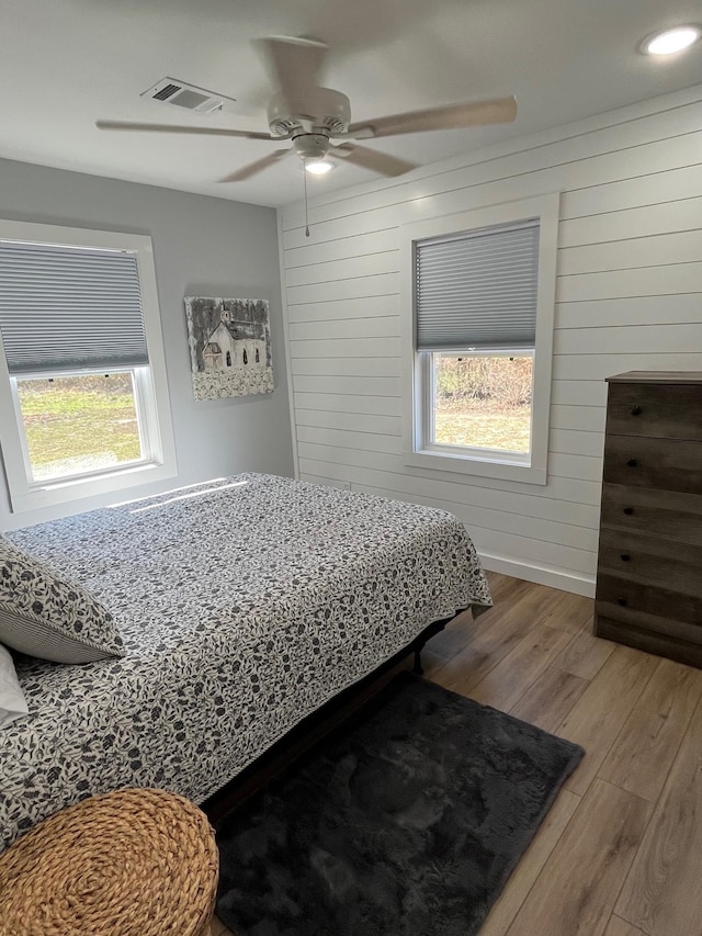 bedroom with ceiling fan, hardwood / wood-style floors, multiple windows, and wood walls