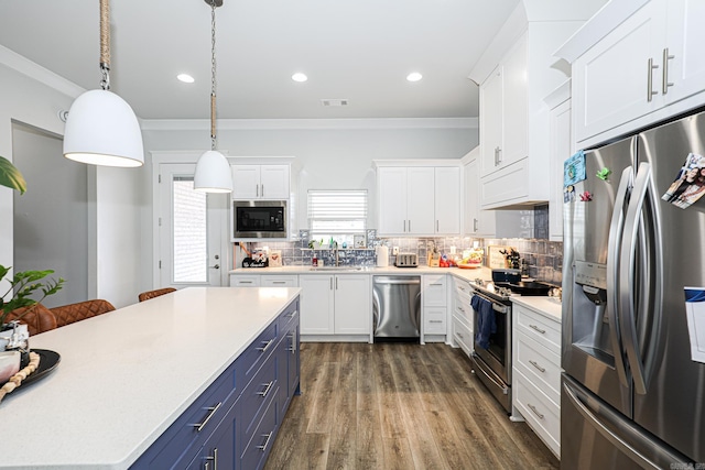 kitchen with appliances with stainless steel finishes, pendant lighting, white cabinetry, crown molding, and blue cabinetry