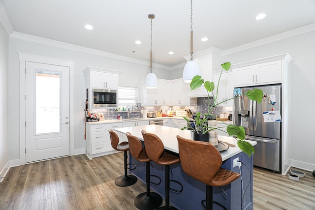 kitchen featuring pendant lighting, appliances with stainless steel finishes, a center island, ornamental molding, and white cabinets