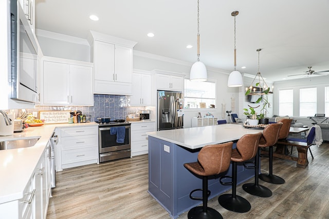 kitchen featuring sink, appliances with stainless steel finishes, white cabinetry, hanging light fixtures, and a kitchen island