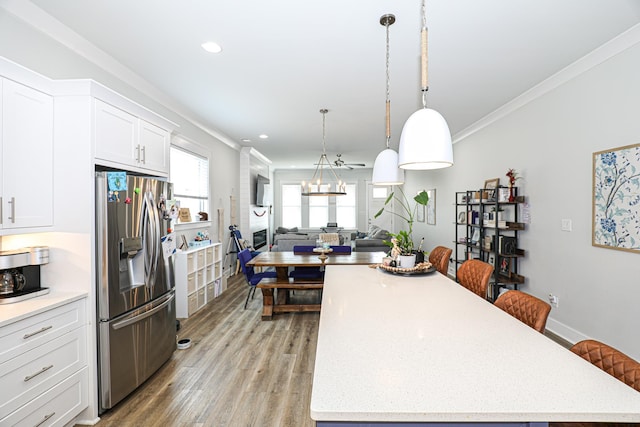 kitchen with stainless steel refrigerator with ice dispenser, a kitchen bar, white cabinetry, light hardwood / wood-style flooring, and ornamental molding