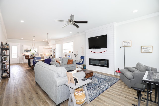 living room with a fireplace, wood-type flooring, ornamental molding, and ceiling fan