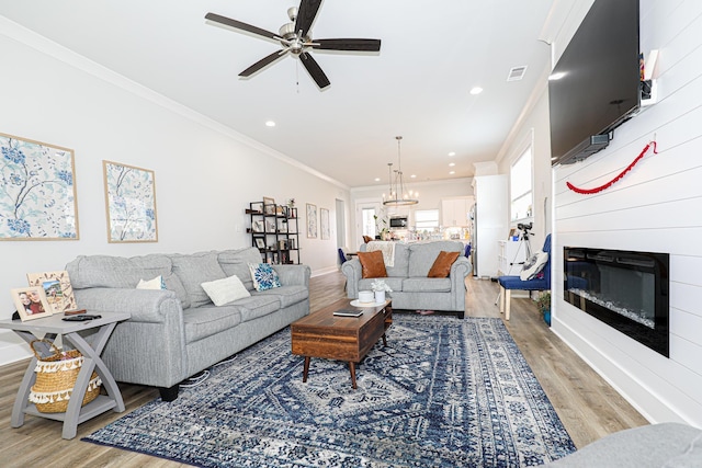 living room with hardwood / wood-style floors, crown molding, ceiling fan with notable chandelier, and a large fireplace