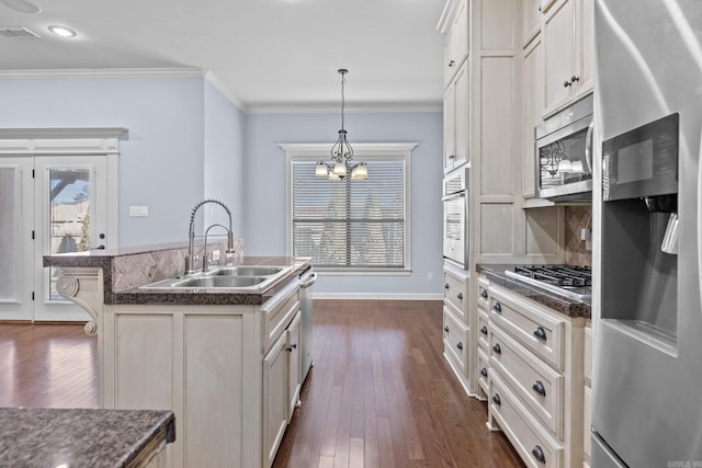 kitchen featuring appliances with stainless steel finishes, an island with sink, sink, decorative backsplash, and hanging light fixtures