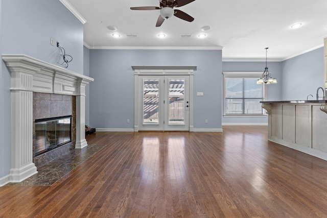 unfurnished living room featuring dark wood-type flooring, ornamental molding, a tiled fireplace, and ceiling fan with notable chandelier