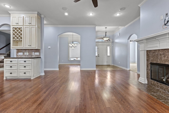 unfurnished living room featuring dark wood-type flooring, ceiling fan, a fireplace, and crown molding