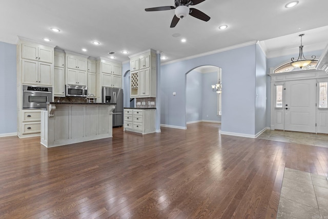 kitchen featuring appliances with stainless steel finishes, an island with sink, backsplash, hanging light fixtures, and dark wood-type flooring