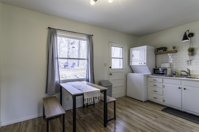 kitchen with light wood-type flooring, stacked washer and clothes dryer, sink, and white cabinets