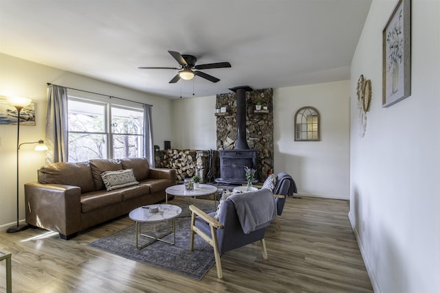 living room with ceiling fan, wood-type flooring, and a wood stove