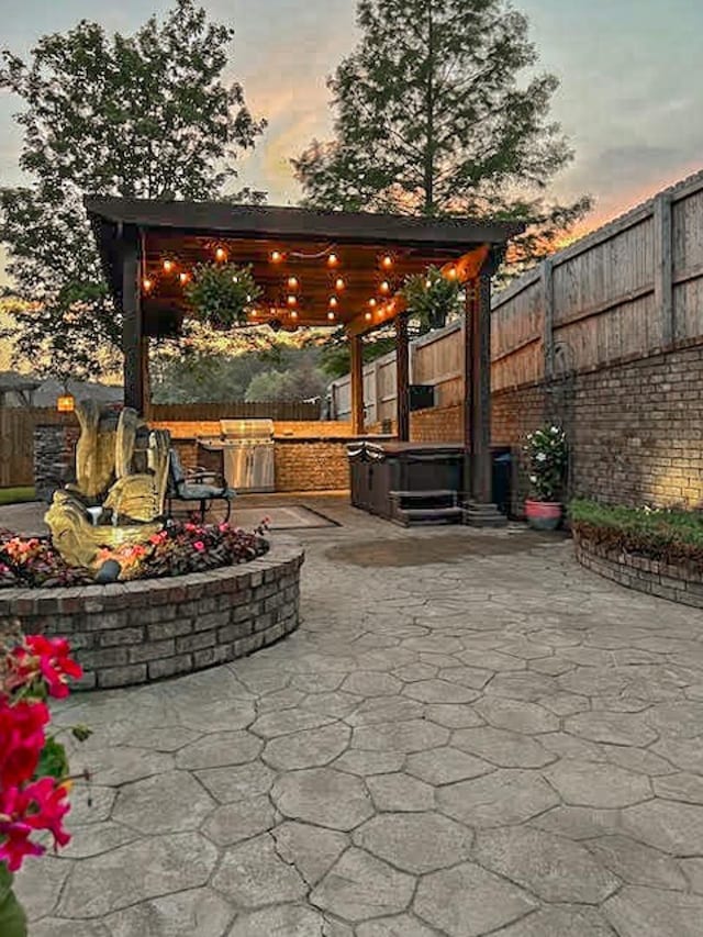 patio terrace at dusk with a gazebo, a hot tub, and exterior kitchen