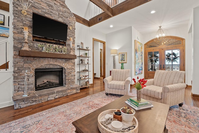 living room with a towering ceiling, dark hardwood / wood-style floors, a fireplace, an inviting chandelier, and french doors