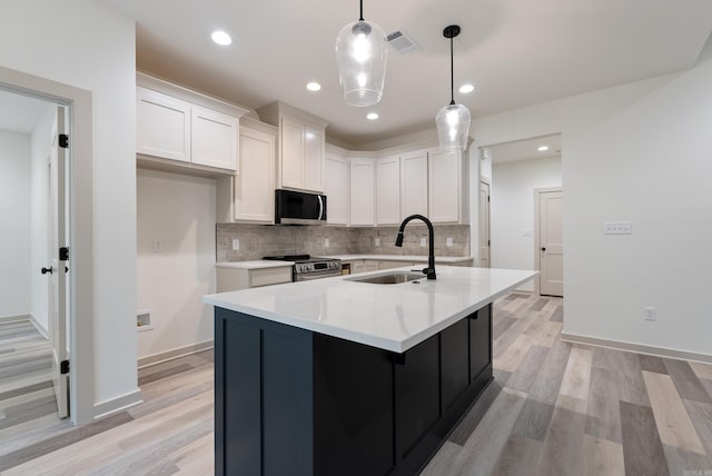 kitchen featuring sink, white cabinetry, a center island with sink, appliances with stainless steel finishes, and pendant lighting