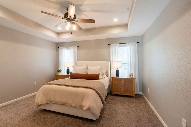 bedroom featuring ceiling fan, a tray ceiling, and carpet