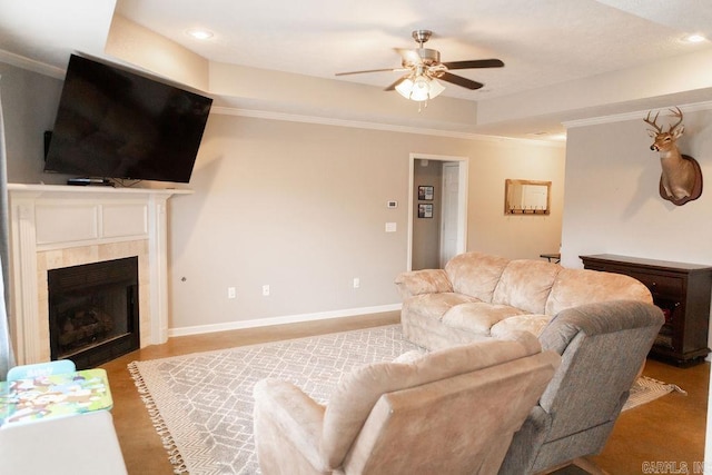 living room with a tiled fireplace, a raised ceiling, ceiling fan, and crown molding