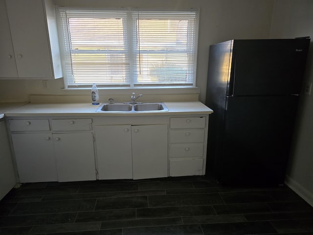 kitchen with white cabinetry, sink, and black fridge