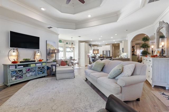 living room featuring ceiling fan with notable chandelier, light hardwood / wood-style flooring, ornamental molding, and a raised ceiling