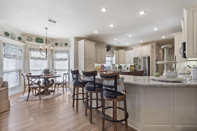 kitchen featuring crown molding, appliances with stainless steel finishes, hanging light fixtures, light stone countertops, and a kitchen bar